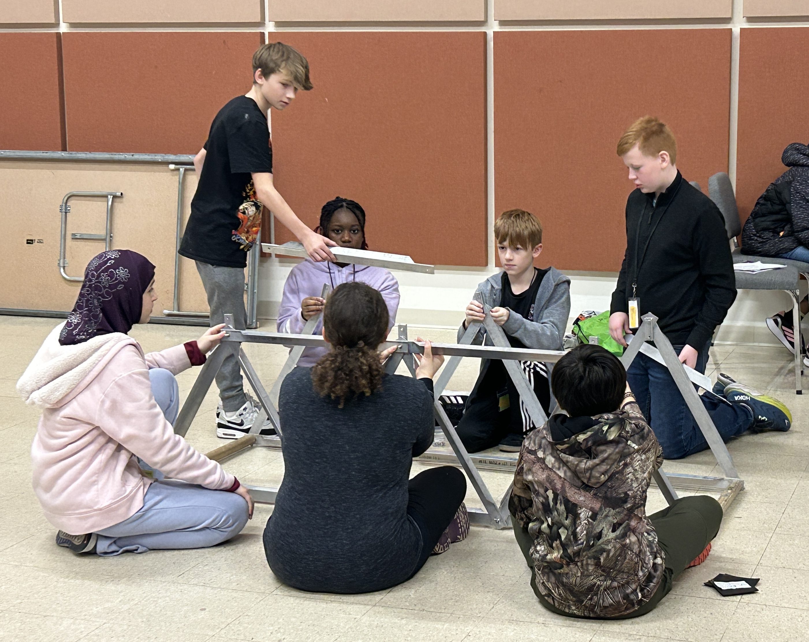 A group of students are building a bridge project together indoors.