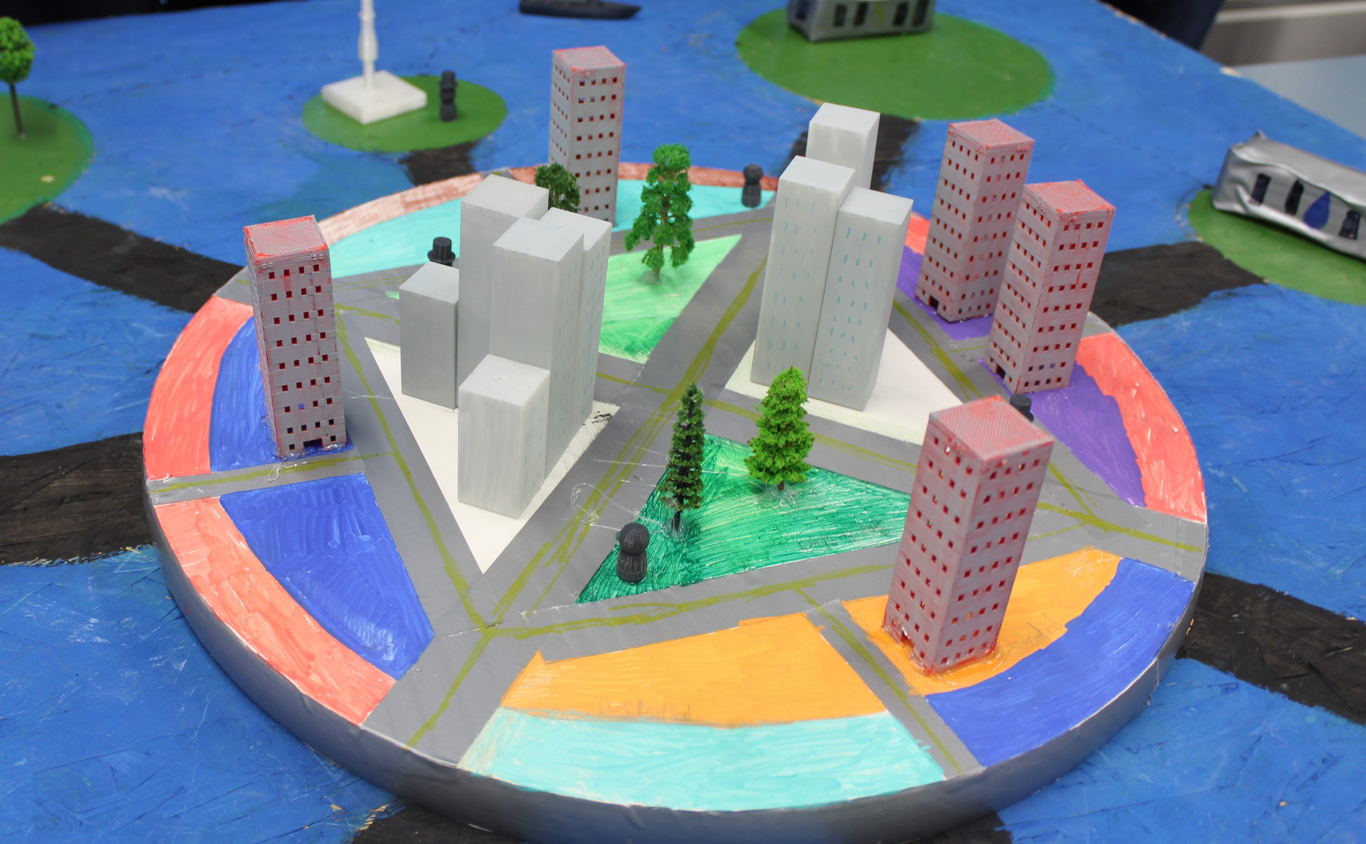 Model of a city with buildings, trees, and roads on a colorful circular base.
