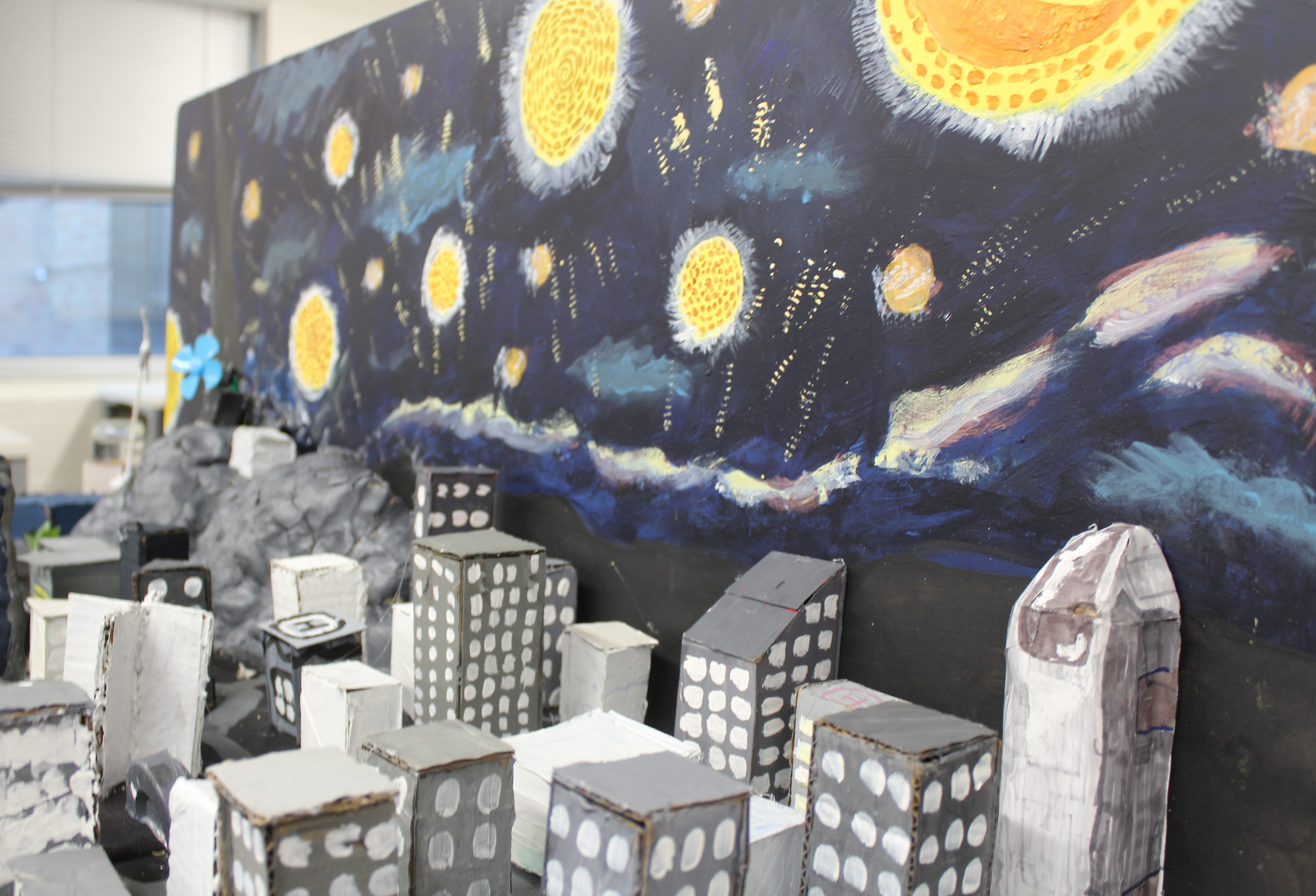 Starry Night-inspired cityscape with painted starry sky and cardboard skyscrapers in a classroom setting.