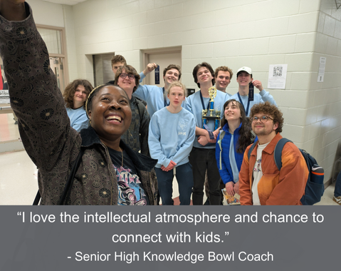 A group of Knowledge Bowl players and two coaches take a selfie, holding a trophy, smiling in a school hallway.
