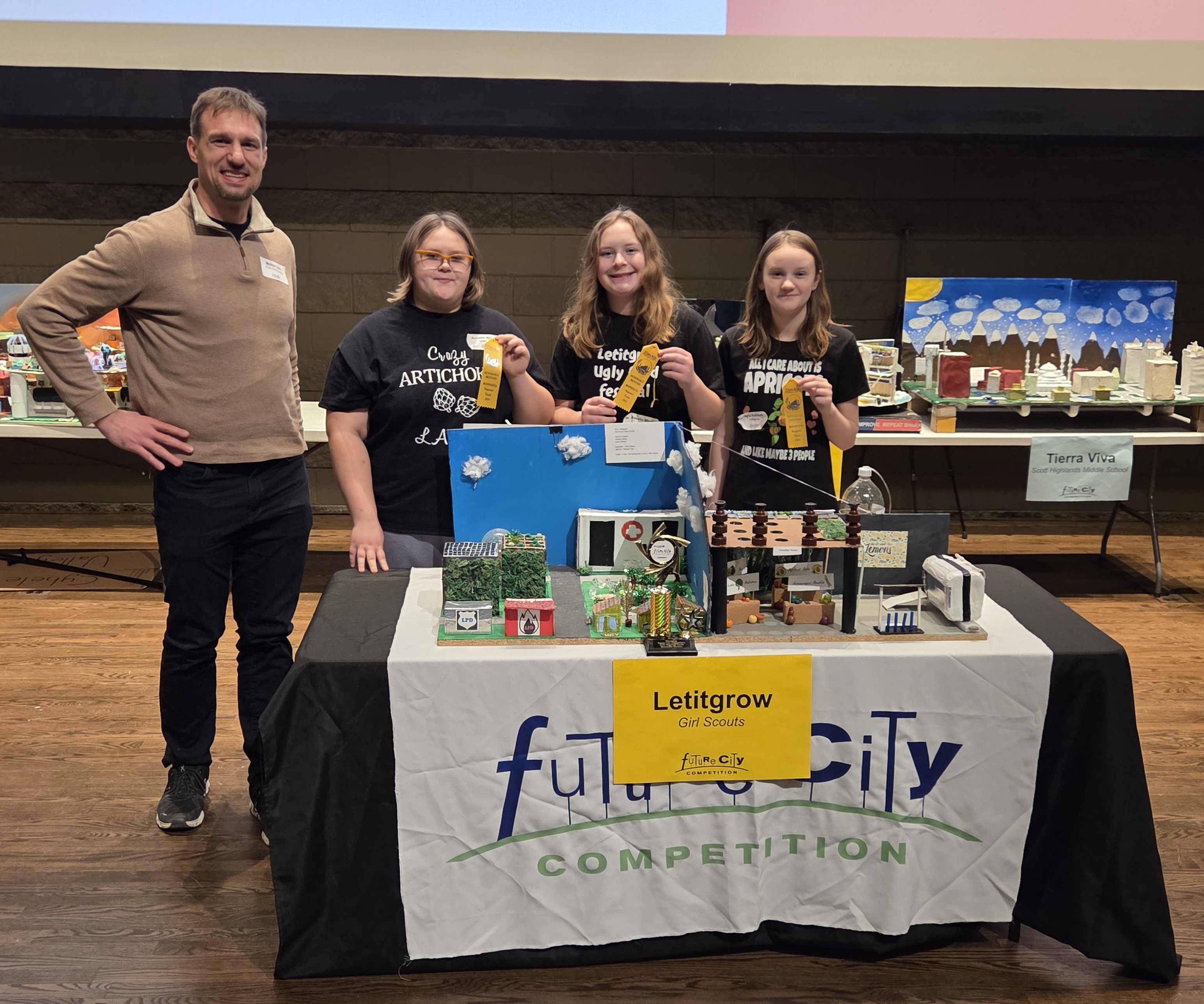 Four people stand behind a table display labeled "Lettigrow" at a Future City competition.