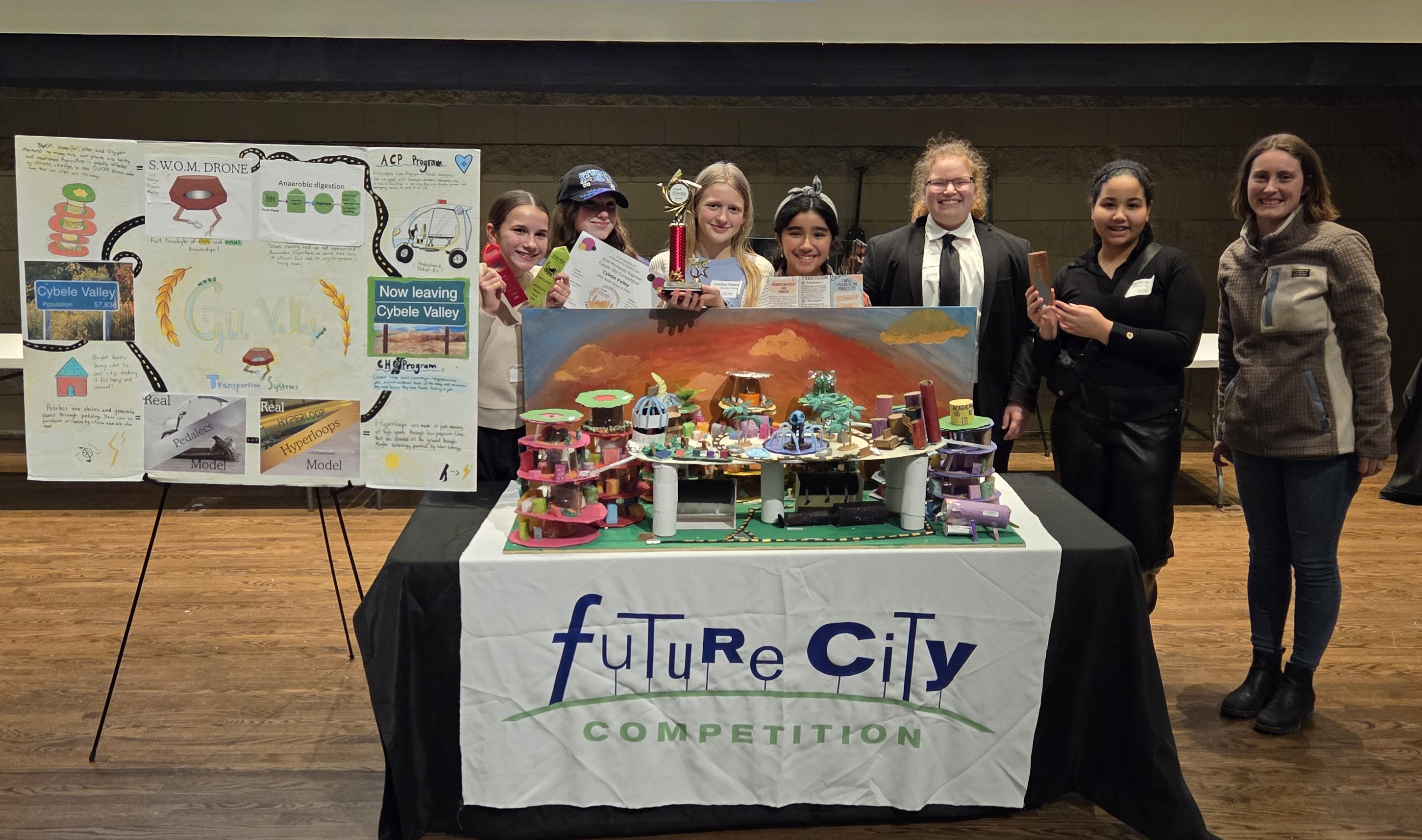 Eight students stand behind a table with a city model and a “Future City Competition” sign.