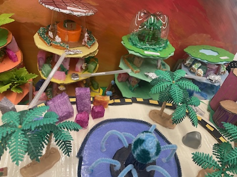 Colorful diorama of a futuristic city with multi-level buildings, palm trees, and a central pool with a sculpture.