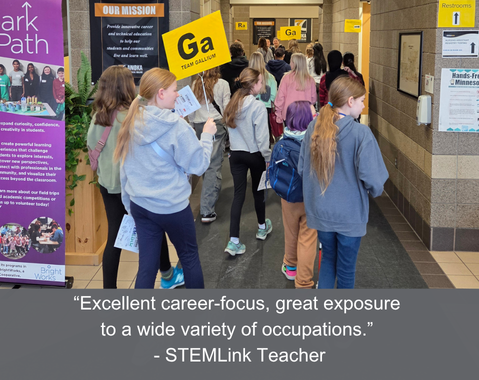 Students walk down a school hallway holding yellow "Ga" team signs at a career-focused STEM event.
