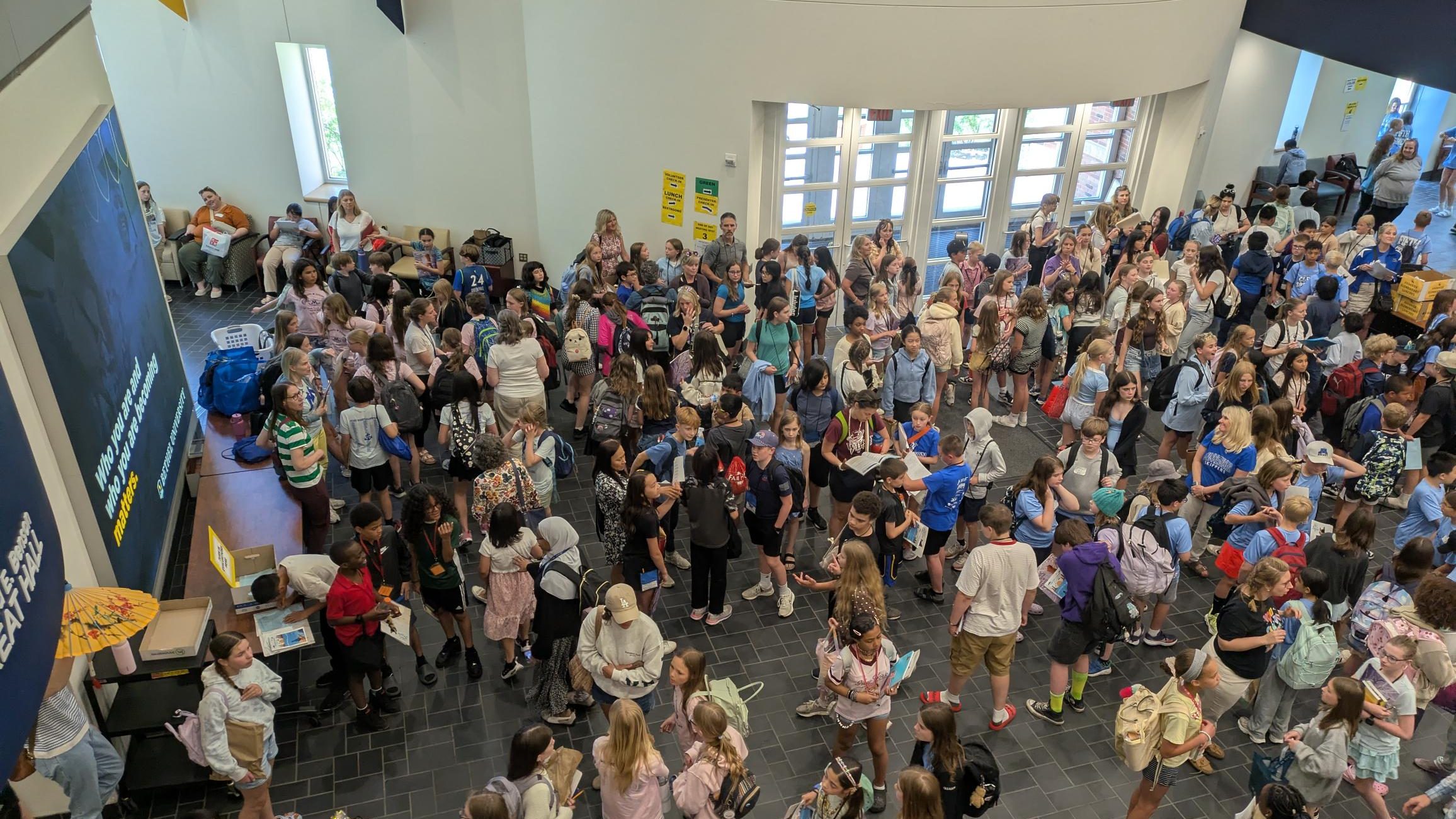 Large crowd of students with backpacks gathered inside a school building, seen from above.